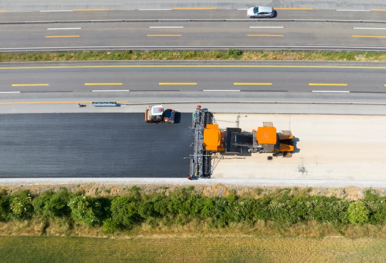 Arbeiter verlegen frischen Asphalt für den Ausbau der Straße.